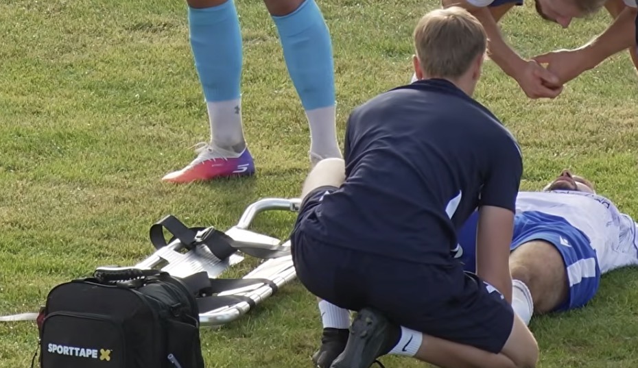 Sports therapist assessing an injured player pitchside, stretcher ready