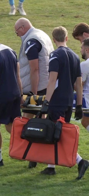 Sports therapist carrying the trauma kit and stretcher onto the pitch
